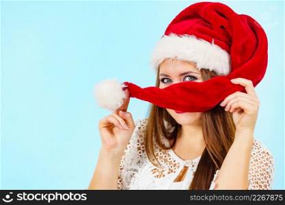 woman wearing santa claus hides her face behind cap. Christmas holiday season. Blue background.. Happy woman in christmas santa hat