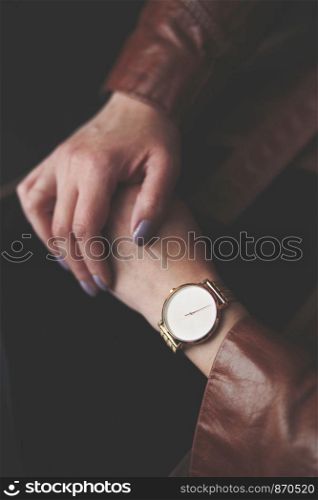Woman wearing silver wristwatch and brown leather coat. Closeup of hands from above