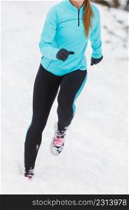 Woman wearing sportswear, running on snow with trees in background, no face, front view. Winter sports, outdoor fitness, health concept.. Running lady legs, sporty clothes, winter fitness