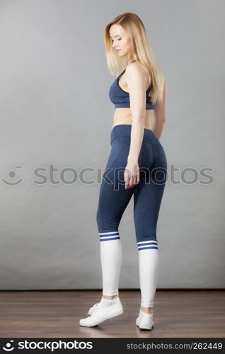 Woman wearing sporty workout outfit, blue sport bra, leggings, socks and trainers. Indoor shot on grey background.. Woman wearing sporty workout outfit