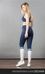 Woman wearing sporty workout outfit, blue sport bra, leggings, socks and trainers. Indoor shot on grey background.. Woman wearing sporty workout outfit