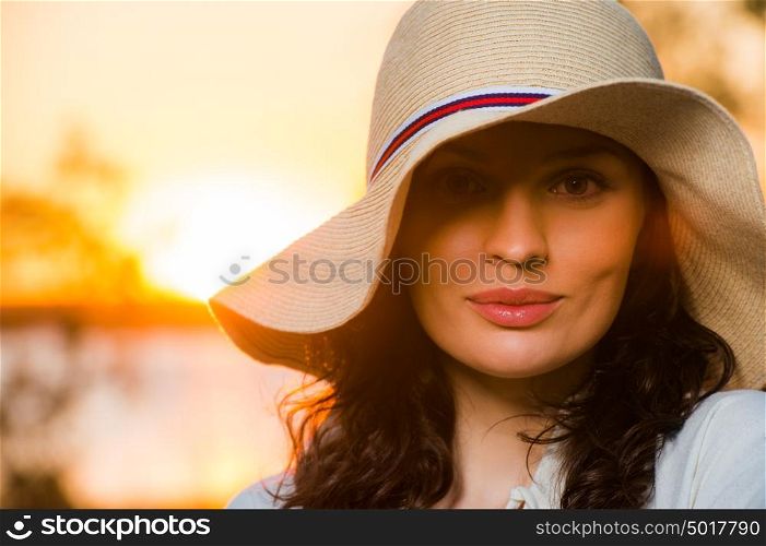 Woman wearing straw hat smiling and having fun against sunset and beautiful sea