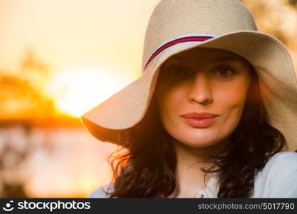 Woman wearing straw hat smiling and having fun against sunset and beautiful sea