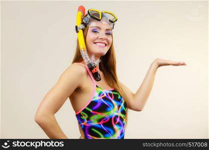 Woman wearing swimsuit with snorkeling mask holding open hand copy space for product, on gray, Smiling girl dreaming about active summer vacation. Snorkeling swimming concept. Woman with snorkeling mask having fun