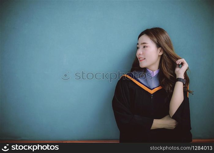 woman wearing university graduation suit standing against clear blue wall toothy smiling face with happiness emotion