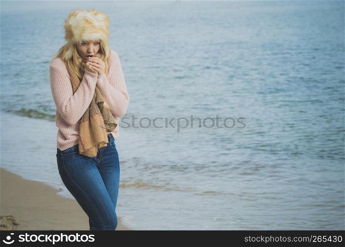 Woman wearing warm stylish autumnal outfit with furry big hat yet feeling cold. Female having chills while relaxing walking on beach.. Woman in stylish outfit feeling cold by the sea