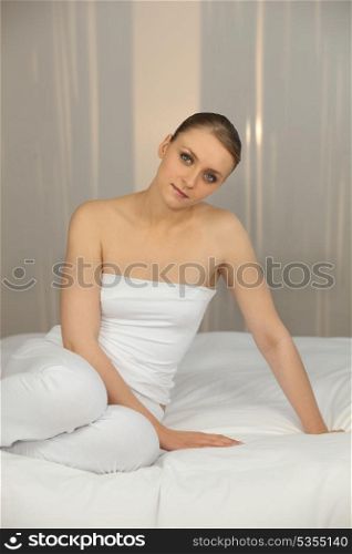Woman wearing white sitting on a white bed