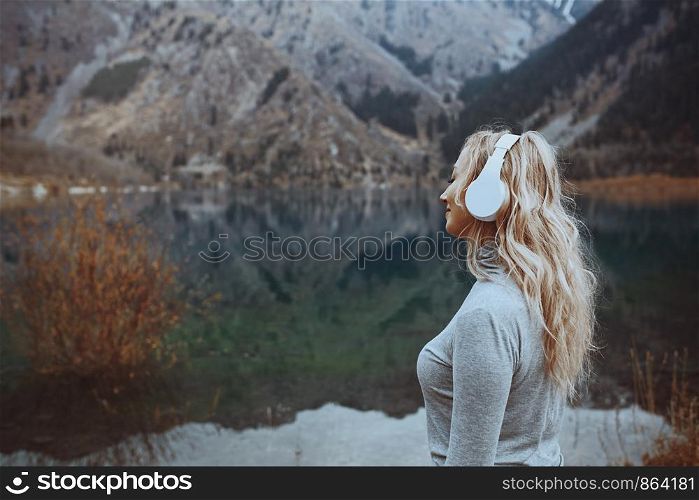 Woman wearing wireless headphones at the mountain lake