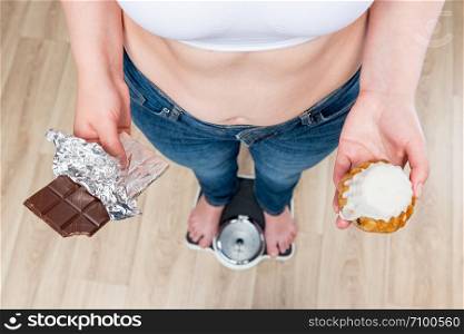 woman weighs on scales, chocolate in her hands and donut