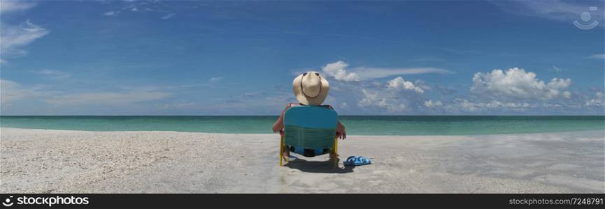 Woman wering sun hat seating in chair sunbathing by waters edge
