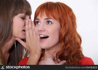 Woman whispering into another woman&rsquo;s ear