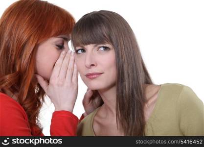 Woman whispering into her friend&rsquo;s ear