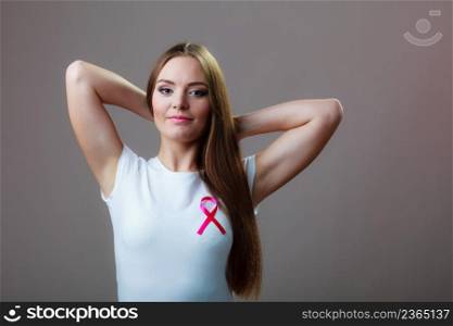 Woman wih pink cancer ribbon on chest. Healthcare, medicine and breast cancer awareness concept. Studio shot, grey background. Woman wih pink cancer ribbon on chest
