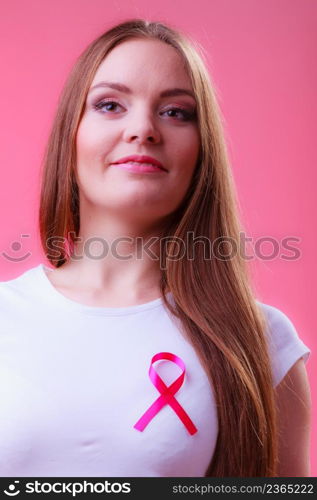 Woman wih pink cancer ribbon on chest. Healthcare, medicine and breast cancer awareness concept. Studio shot, red background. Woman wih pink cancer ribbon on chest