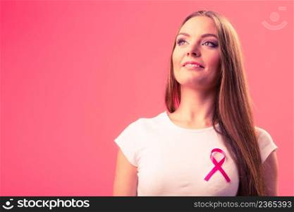 Woman wih pink cancer ribbon on chest. Healthcare, medicine and breast cancer awareness concept. Studio shot, red background. Woman wih pink cancer ribbon on chest