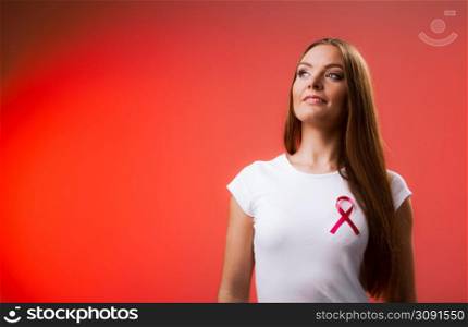 Woman wih pink cancer ribbon on chest. Healthcare, medicine and breast cancer awareness concept. Studio shot, red background. Woman wih pink cancer ribbon on chest