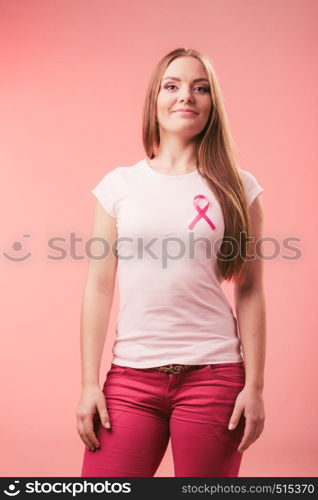 Woman wih pink cancer ribbon on chest. Healthcare, medicine and breast cancer awareness concept. Studio shot, red background. Woman wih pink cancer ribbon on chest