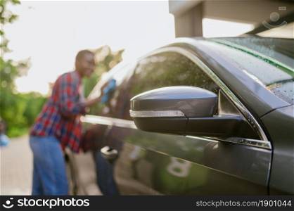Woman wipes a car with a rag, hand auto wash station. Car-wash industry or business. Female person cleans her vehicle outdoors. Woman wipes a car with rag, hand auto wash