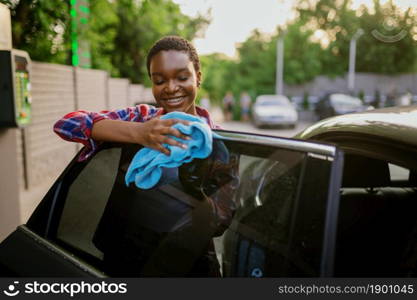 Woman wipes a car with a rag, hand auto wash station. Car-wash industry or business. Female person cleans her vehicle outdoors. Woman wipes a car with rag, hand auto wash