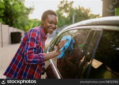 Woman wipes a car with a rag, hand auto wash station. Car-wash industry or business. Female person cleans her vehicle from dirt outdoors. Woman wipes a car with rag, hand auto wash