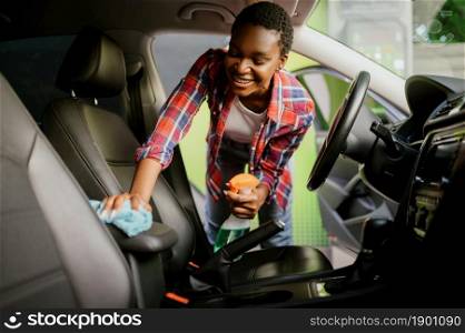 Woman wipes car interior with a rag, hand auto wash station. Car-wash industry or business. Female person cleans her vehicle from dirt outdoors. Woman wipes car interior with rag, hand auto wash