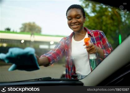 Woman wipes car window with a rag, hand auto wash station. Car-wash industry or business. Female person cleans her vehicle from dirt outdoors. Woman wipes car window with a rag, hand auto wash