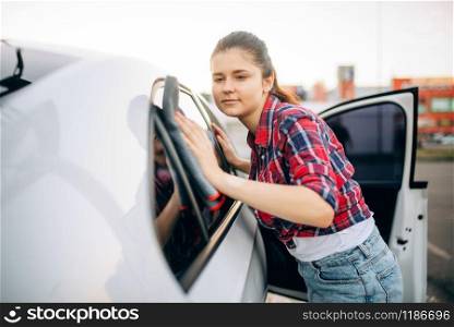 Woman wipes the car with a cloth after washing, polishing process on self-service car-wash. Lady cleaning vehicle. Woman wipes the car with a cloth after washing