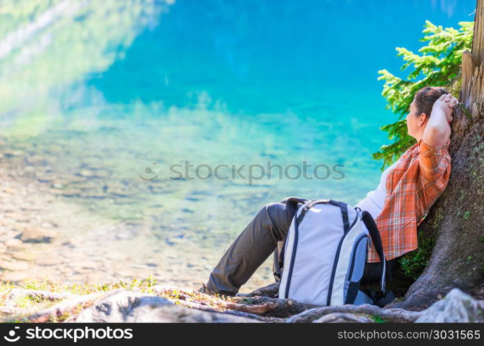 woman with a backpack relaxes and rests by the lake in the mount. woman with a backpack relaxes and rests by the lake in the mountains