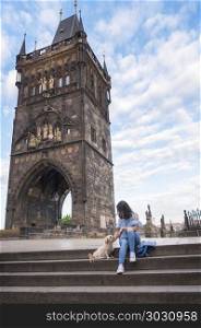 Woman with a dog in front of the tower of Charles Bridge. Young brunette girl petting her dog on the stairs in front of the tower on the Charles Bridge, in the old town of Prague, in the Czech Republic.