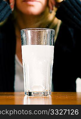 Woman with a very bad hangover or migraine headache sitting in front of a glass of water with a painkiller