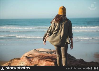 Woman with a yellow cap and walking over a cliff to see the beach