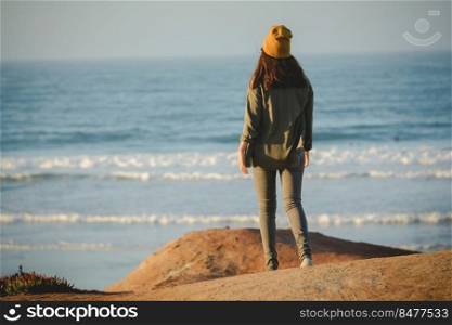 Woman with a yellow cap and walking over a cliff to see the beach