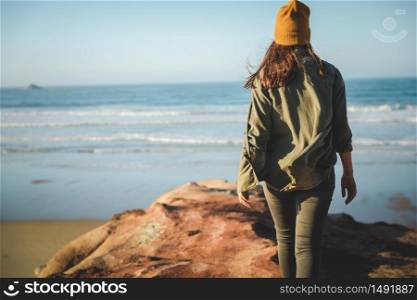 Woman with a yellow cap and walking over the cliff to see the beach