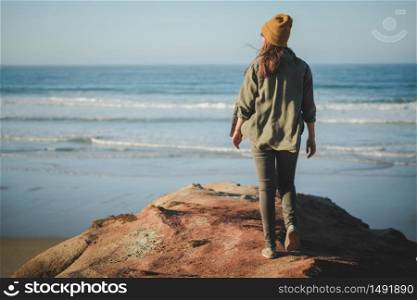 Woman with a yellow cap and walking over the cliff to see the beach