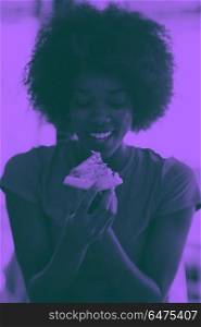 woman with afro hairstyle eating tasty pizza slice. young very hangry african american woman with afro hairstyle eating tasty pizza slice in fast food restaurant duo tone filter