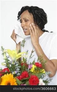Woman with allergy holding tissue, near flowers, studio shot
