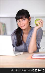 Woman with an apple sitting at her laptop