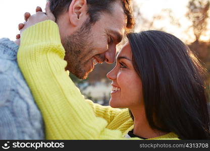 Woman with arms around man face to face smiling