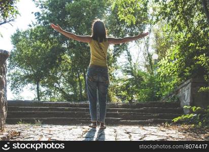 Woman with arms outstretched against sun in the park
