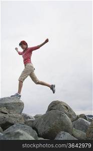Woman with arms outstretched, jumping on rocks