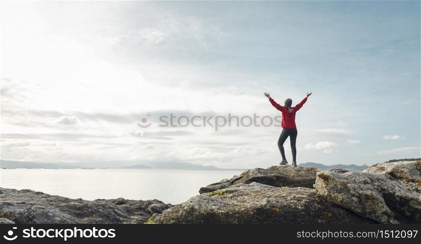 Woman with arms raised enjoying the beautiful morning view of the coast