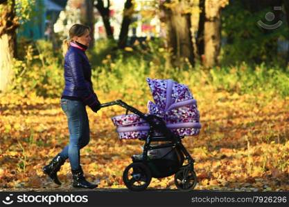 woman with baby in perambulator walking in the autumn park