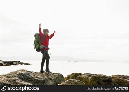 Woman with backpack and arms raised  enjoying the beautiful morning view of the coast