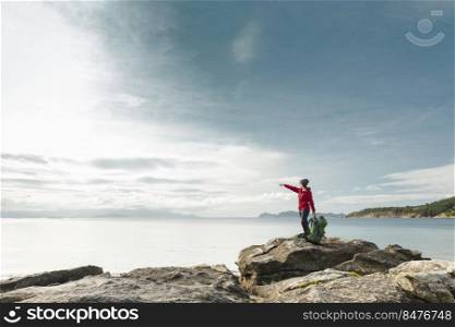 Woman with backpack enjoying and pointing to the beautiful morning view of the coast