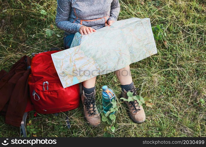 Woman with backpack having break during trip in mountains looking at map sitting on grass on summer vacation day