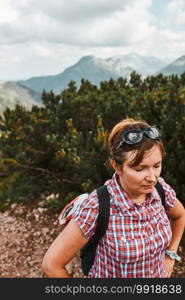 Woman with backpack hiking in a mountains, actively spending summer vacation, having break after going up on a hill standing on mountain path by mugo pine. Woman with backpack hiking in a mountains, actively spending summer vacation, having break after going up on a hill