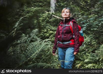 Woman with backpack hiking in forest, actively spending summer vacation close to nature. Woman walking on path among trees