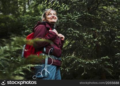 Woman with backpack hiking in forest, actively spending summer vacation close to nature. Woman walking on path among trees