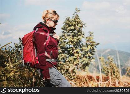 Woman with backpack hiking in mountains, spending summer vacation close to nature. Woman walking on path among bushes and grass