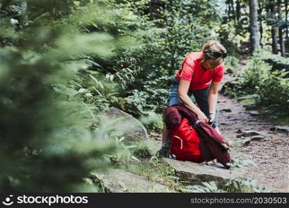 Woman with backpack hiking in mountains, spending summer vacation close to nature. Woman walking on path among bushes and trees